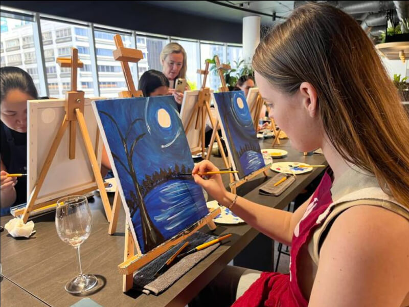 Woman painting a canvas with a glass of wine in a paint and sip class